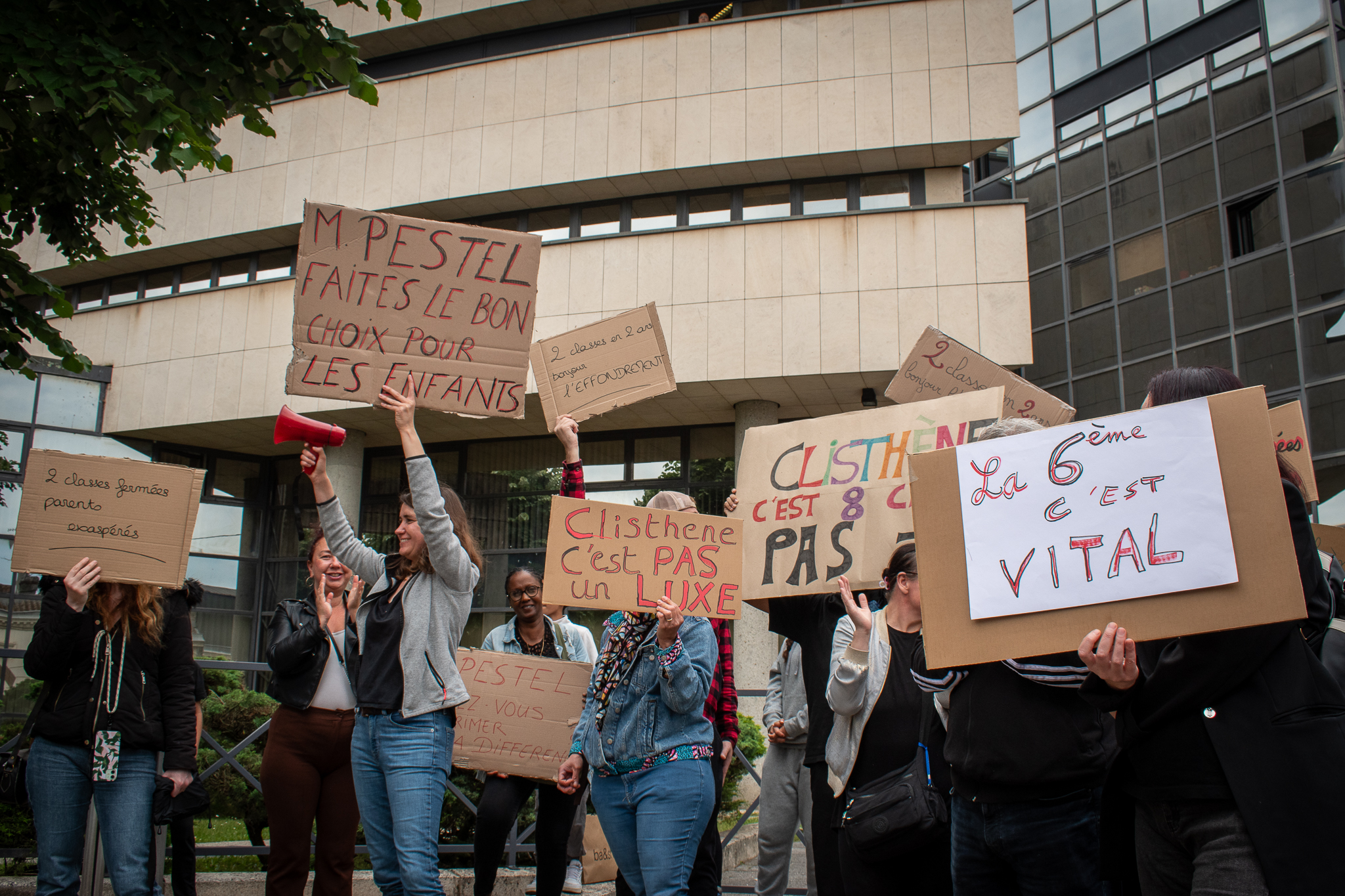 Photo montrant un rassemblement devant la Direction des Services Départementaux de l’Éducation Nationale de la Gironde (DSDEN 33) à Bordeaux. Une cinquantaine de parents, élèves et professeurs du collège Clisthène manifestent contre la fermeture d’une classe de sixième dans cet établissement scolaire expérimental. Pancartes, banderoles et expressions de mécontentement soulignent la mobilisation contre cette décision.