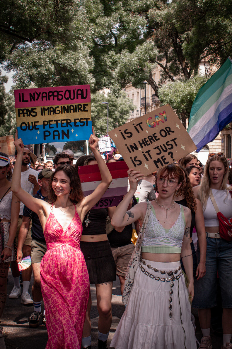 Participants et participantes de la Pride 2025 à Bordeaux défilent dans les rues, arborant drapeaux arc-en-ciel, pancartes militantes LGBTQIA+ et tenues colorées.