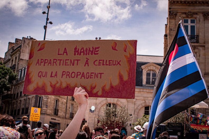 Participants et participantes de la Pride 2025 à Bordeaux défilent dans les rues, arborant drapeaux arc-en-ciel, pancartes militantes LGBTQIA+ et tenues colorées.