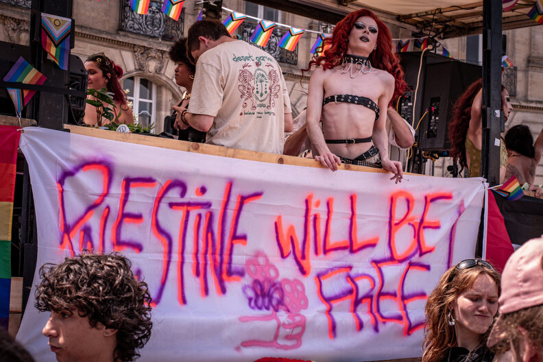 Participants et participantes de la Pride 2025 à Bordeaux défilent dans les rues, arborant drapeaux arc-en-ciel, pancartes militantes LGBTQIA+ et tenues colorées.
