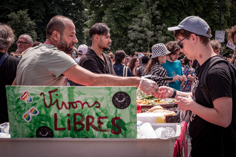 Participants et participantes de la Pride 2025 à Bordeaux défilent dans les rues, arborant drapeaux arc-en-ciel, pancartes militantes LGBTQIA+ et tenues colorées.