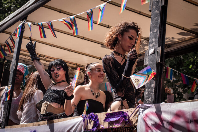 Participants et participantes de la Pride 2025 à Bordeaux défilent dans les rues, arborant drapeaux arc-en-ciel, pancartes militantes LGBTQIA+ et tenues colorées.