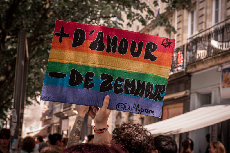 Participants et participantes de la Pride 2025 à Bordeaux défilent dans les rues, arborant drapeaux arc-en-ciel, pancartes militantes LGBTQIA+ et tenues colorées.