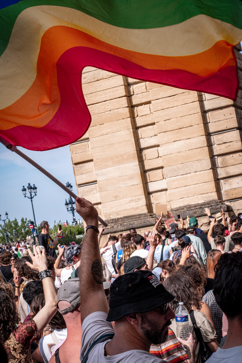 Participants et participantes de la Pride 2025 à Bordeaux défilent dans les rues, arborant drapeaux arc-en-ciel, pancartes militantes LGBTQIA+ et tenues colorées.
