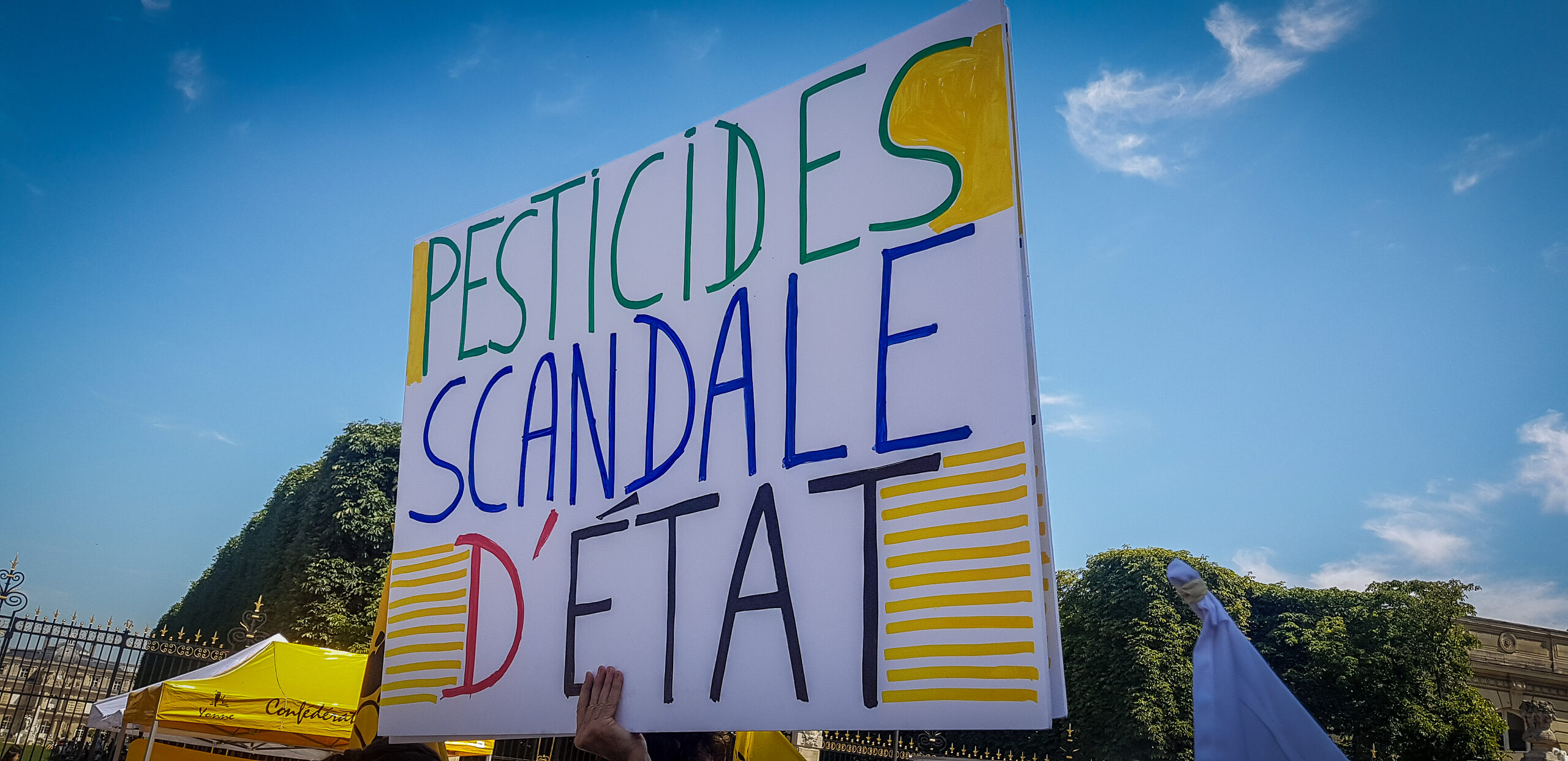 Pancarte lors d’une manifestation contre la loi Duplomb, affichant le message « Pesticides, scandale d’État » sur fond de ciel bleu. Crédit : Jean-Claude Utard (Flickr)